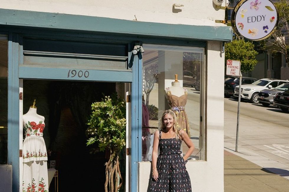 Woman standing outside a boutique called "Eddy" with mannequins in the window.