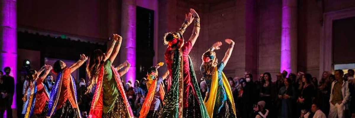 women in Indian saris dancing with their hands up in front of an audience