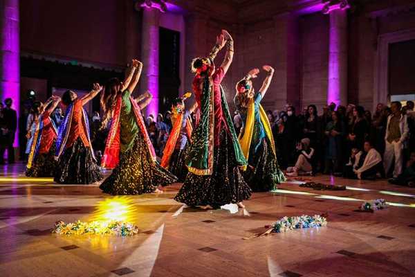 women in Indian saris dancing with their hands up in front of an audience
