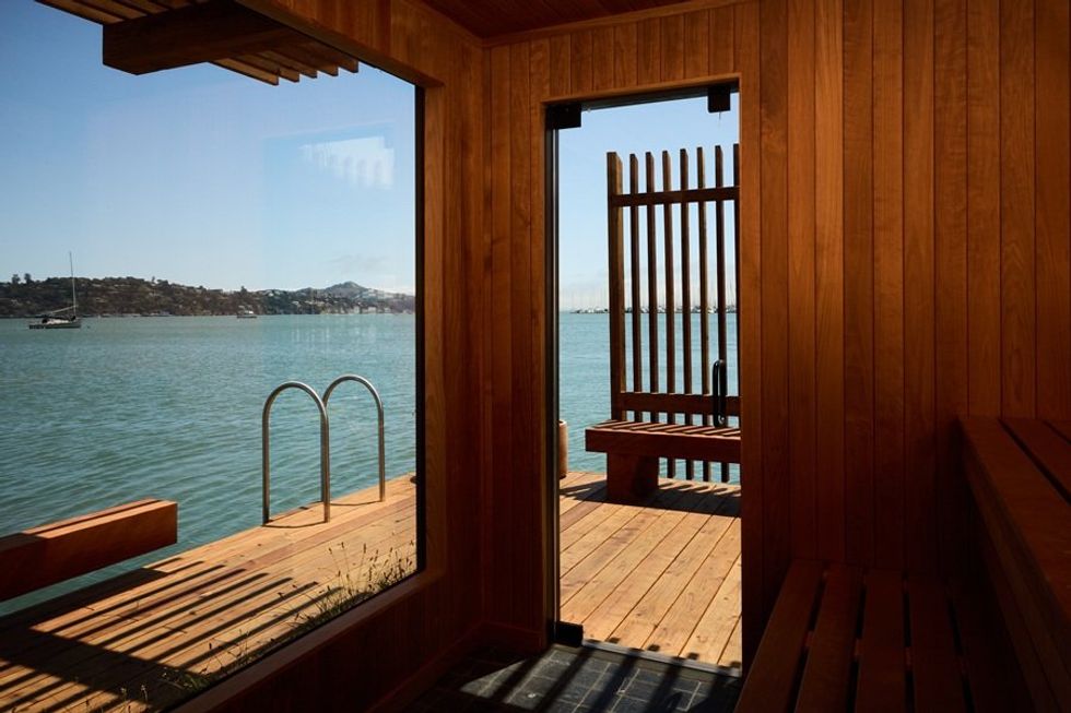 Wooden sauna interior with a view of the sea and distant hills through a large window and door.